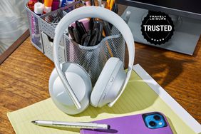 A pair of the best noise cancelling headphones leaned against a pencil holder on a desk with a Travel + Leisure Trusted badge.