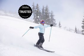 A person smiles while skiing downhill wearing a Stio Shot 7 Down Jacket