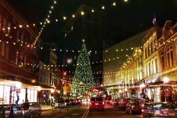 Christmas lights are strung zigzagging from one side of the street to the other, heading to a giant Christmas tree at the intersection.
