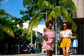 Female friends holding shopping bags and drinks in city. Young women are walking on street during summer. They are enjoying city life on sunny day
