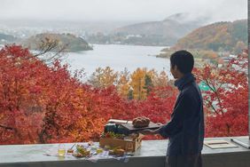 A man stands in front of fiery red autumn foliage from a terrace at the Hoshinoya Fuji resort