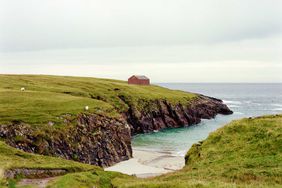 Green cliffs and a beach on the Isle of Lewis in Scotland, with a red house on the cliff