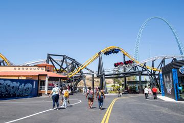 Visitors walk past the West Coast Racers roller coaster at the theme park Six Flags Magic Mountain on the day of the park's re-opening, April 1, 2021, in Valencia, California.