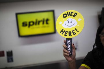 An employee holds a sign to direct travellers at the Spirit Airlines Inc. ticket counter at Fort Lauderdale International Airport (FLL)