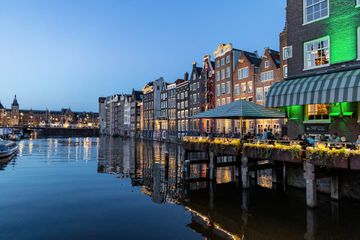 View of the evening city, ships moored on the canal, central railway station in the distance in Amsterdam, The Netherlands 