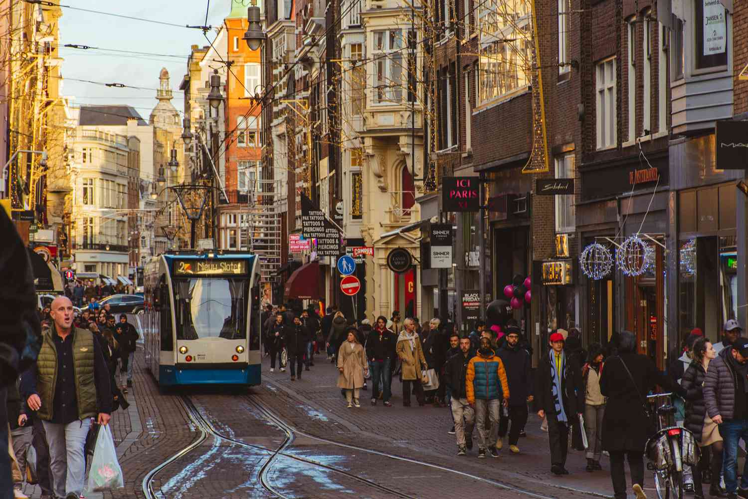 Tram passing by in the streets of Amsterdam while crowd of people are walking and shopping beside - Amsterdam, Netherlands