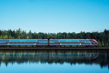 An Amtrak train riding past trees and a lake 