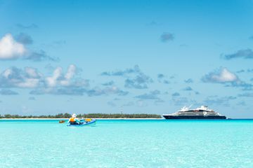 A man kayaks near a cruise ship in the waters of Assumption Island, in the Seychelles