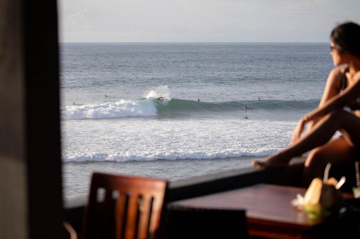 A person blurred in frame looks onto to the surfers on a beach in Bali