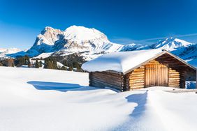 Sunset on Sassopiatto and Sassolungo from wood chalet in the snow, Alpe di Siusi / Seiser Alm, Dolomites, South Tyrol, Italy