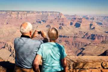 An elderly man photographing while standing with wife at the Grand Canyon 