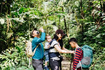 Asian family with a toddler and young child hiking together in a forest