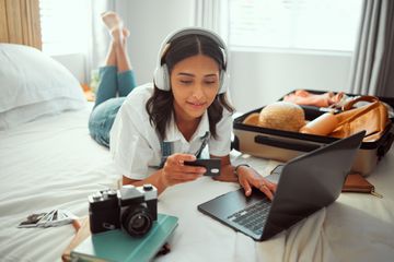 A young adult lays on bed to book travel vacation on their computer
