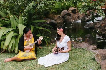 Two women play ukulele beside a pong on a Hawaiian resort