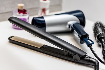 Hair brush, blow dryer and hair straightener on a bathroom countertop 