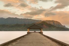 Rising sun illuminates the peaks of Na Pali mountains over the calm bay and Hanalei Pier in long exposure photo