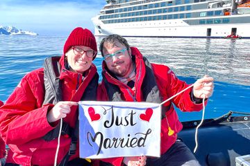 A couple holding up a "just married" sign on a zodiac boat after getting married in Antarctica