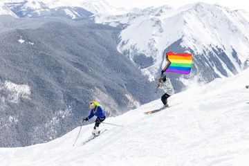 Skiers going down a mountain with the pride flag during Aspen Gay Ski Week