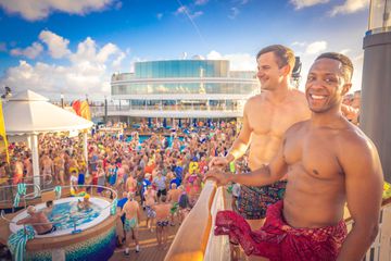 Two men standing on a balcony overlooking a large party on a cruise ship