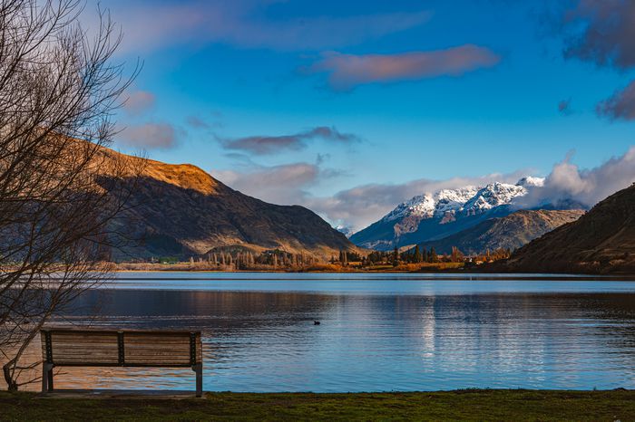 A bench overlooks a lake surrounded by mountains in New Zealand