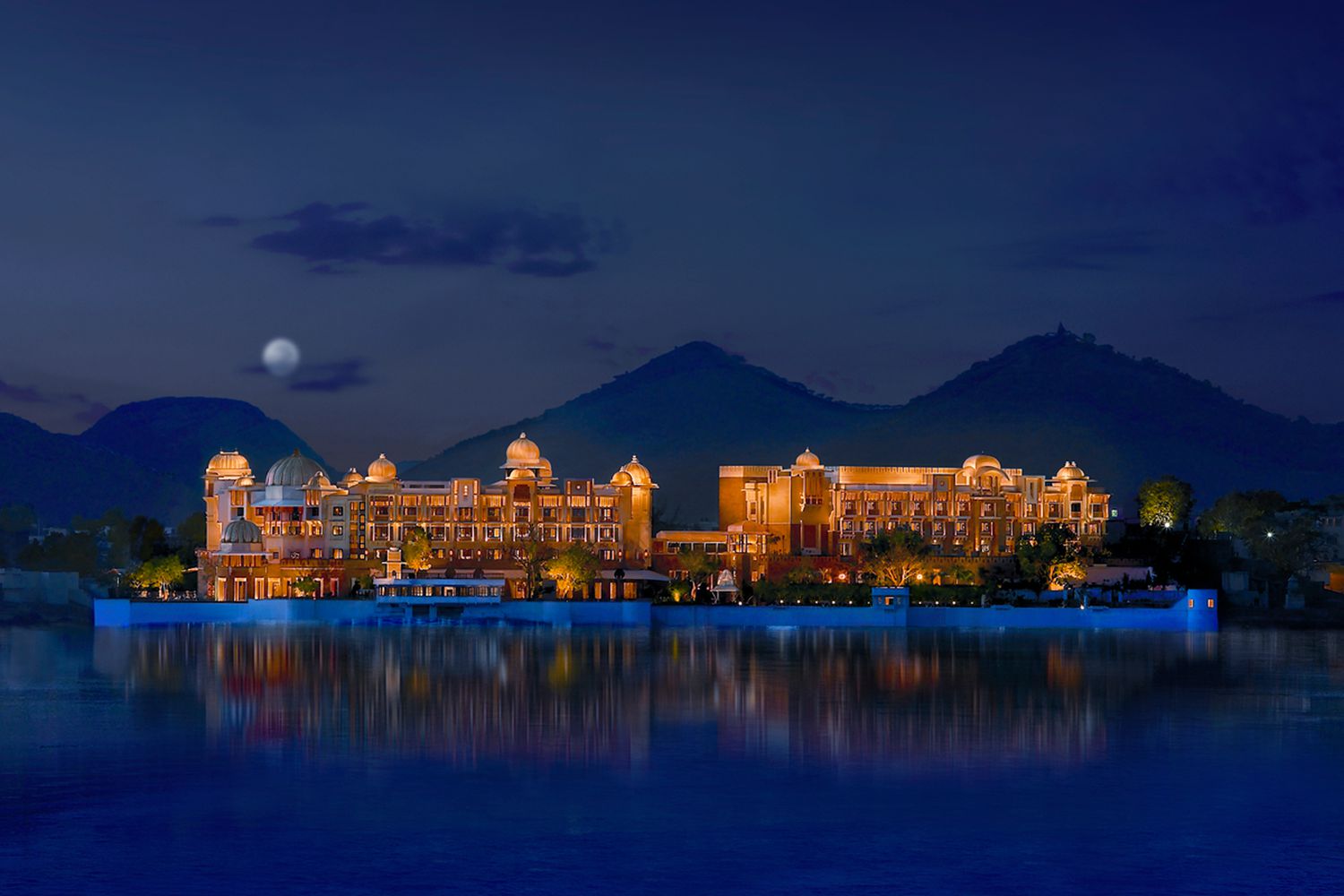 Exterior of the Leela Palace Udaipur at night with the moon and mountains rising behind
