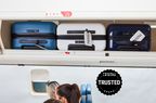 Three pieces of carry-on luggage in an airplane's overhead bin with passengers seated below