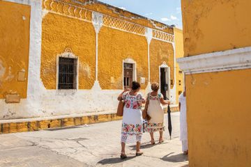 Two women go around a colorful corner in Merida, Mexico