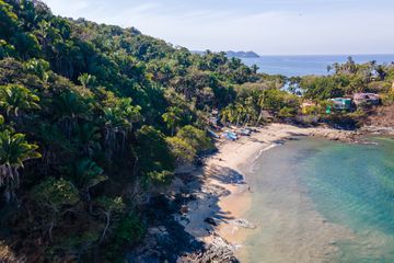 Drone point of view on hidden small beach, surrounded by tropical palm trees in San Pancho, Nayarit, Mexico.