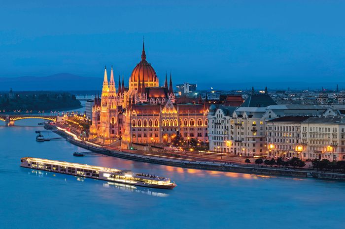 A long cruise ship sails in the waters near old buildings in Budapest