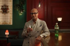 Stanely Tucci raises a martini glass at a bar 