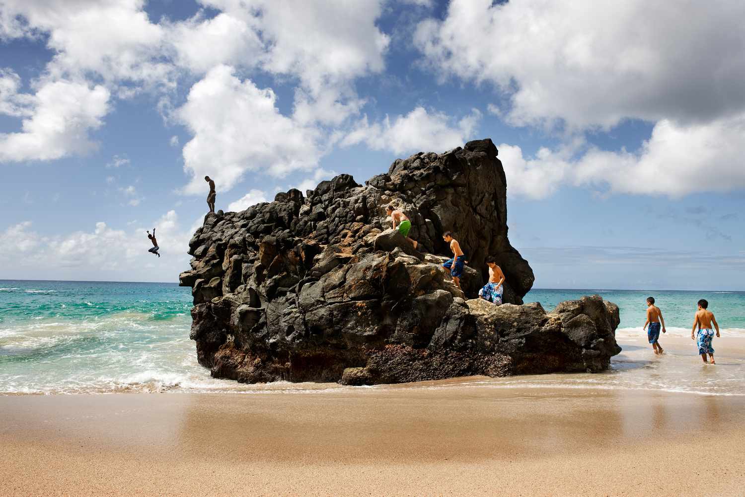 Friends climbing and jumping off rock into ocean