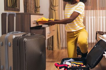 A woman unpacking her suite case into a hotel room dresser 