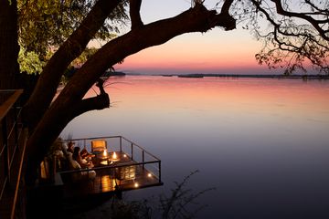 People sit on a deck overlooking a river at sunset