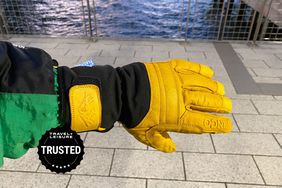 A hand wearing a Kinco Premium Leather Work and Ski Mitt with Nikwax Waterproof Wax with gray tiles in background