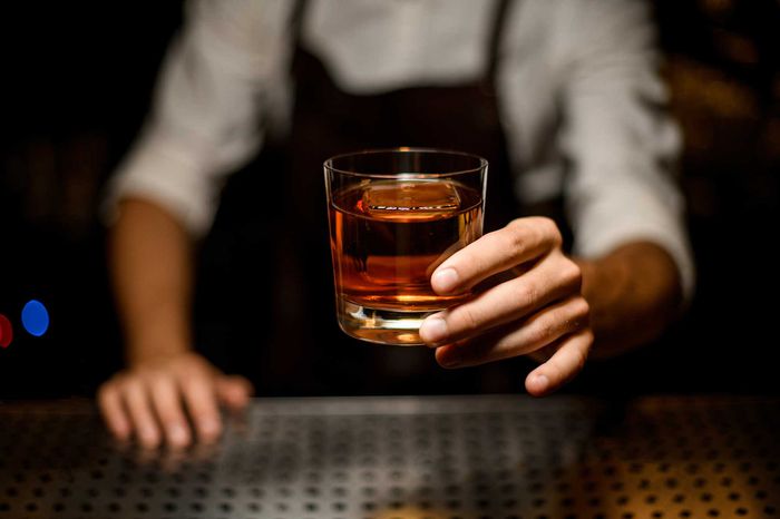 Professional bartender serving a cocktail in the glass with one big ice cube