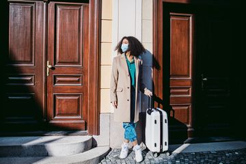 A young woman wearing mask with luggage standing on streets in old town