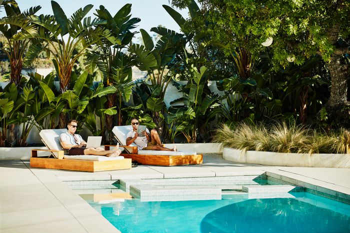 Gay couple working on laptop and digital tablet while relaxing by pool